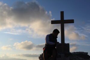 A person sitting on the rock beside wooden cross