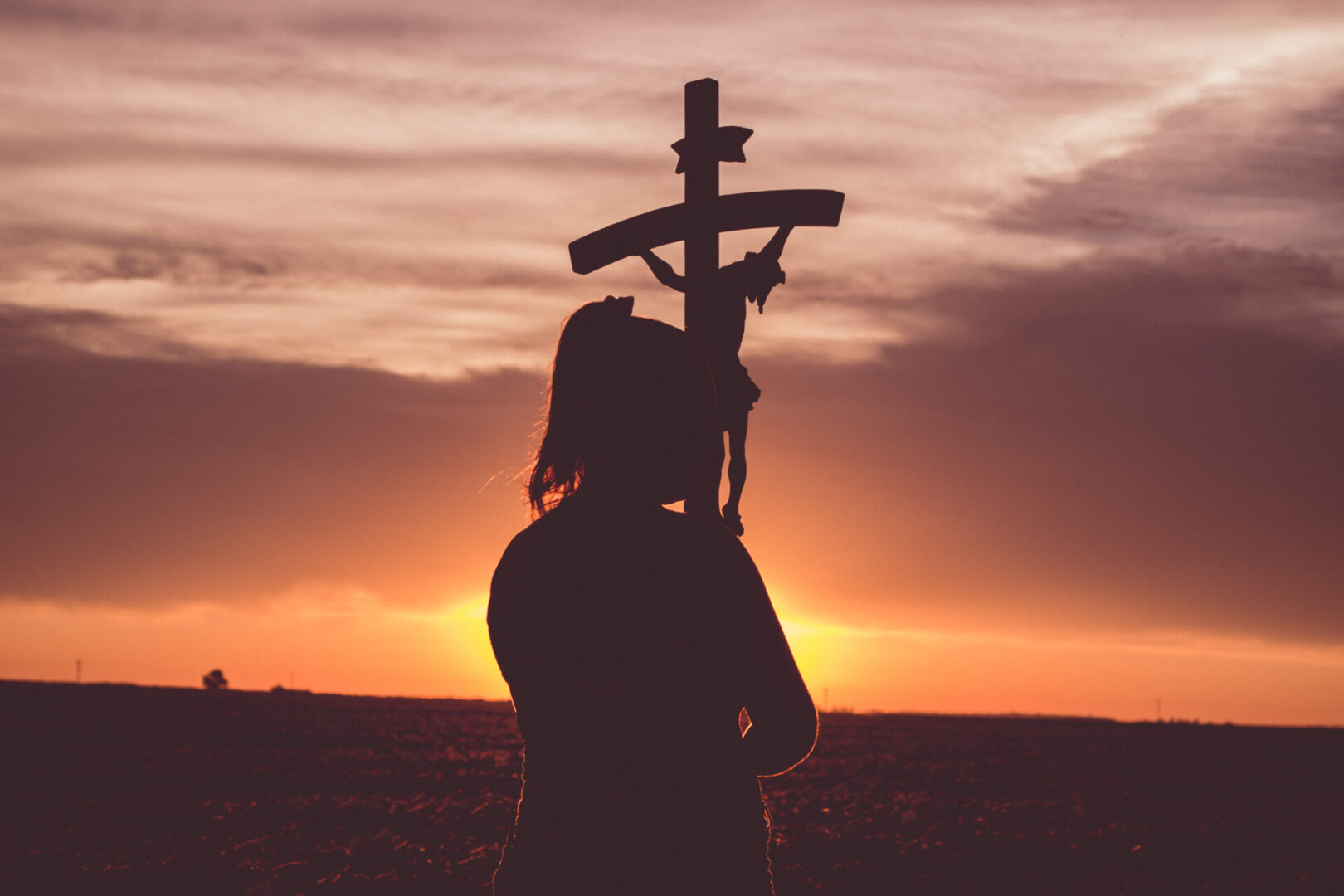 Close shot of a woman holding the crucifix at the sunset