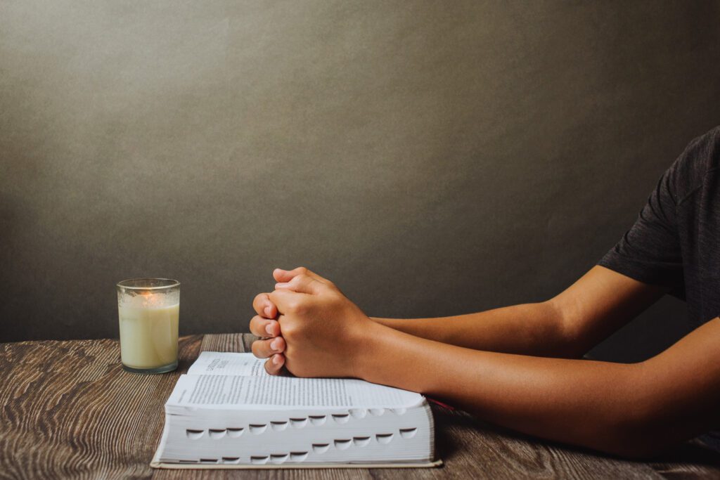 A person hands on the bible and candle on the table