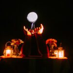 Hands holding glowing orb over candlelit table
